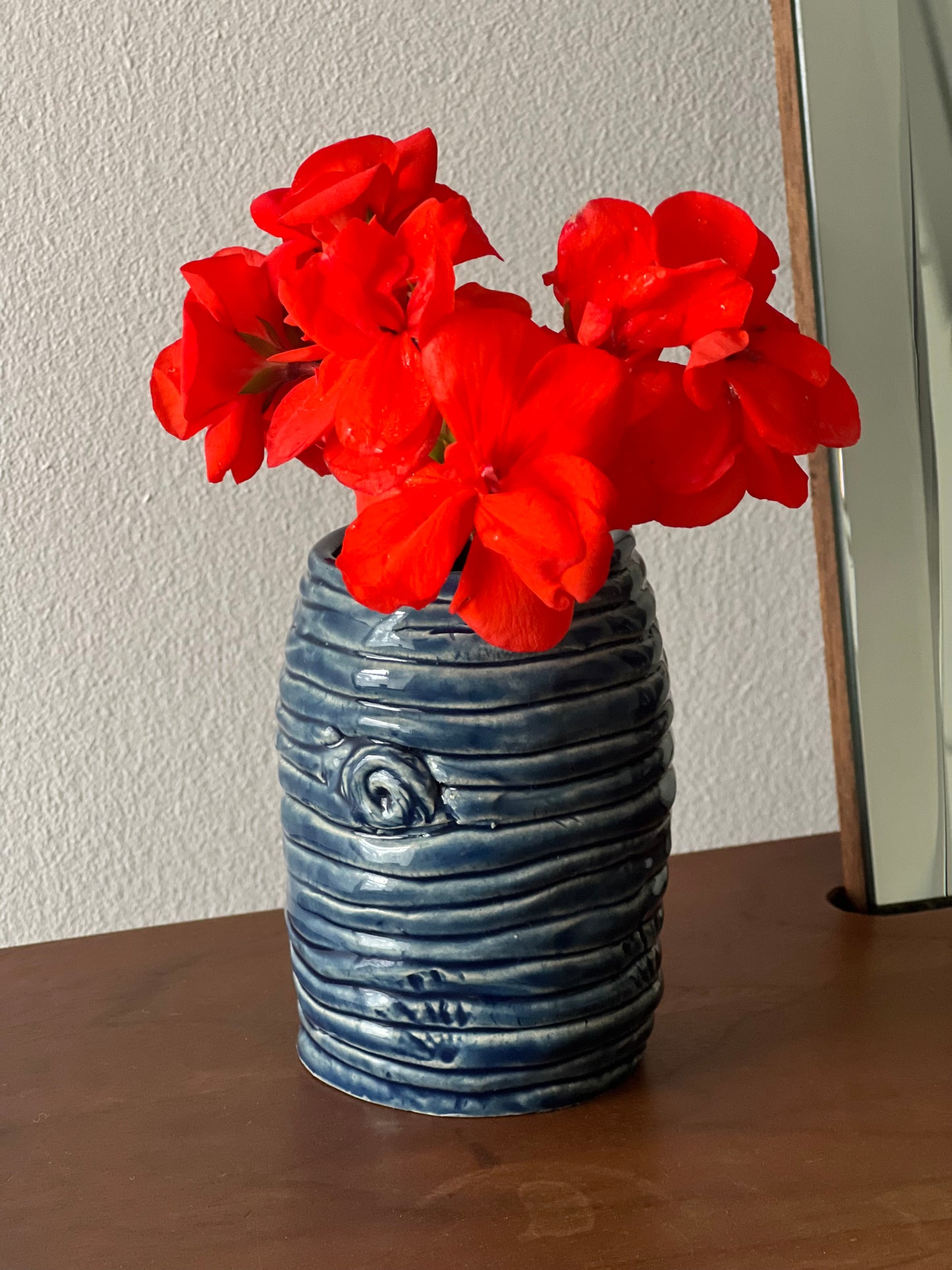 Blue textured vase with red flowers on a wooden surface