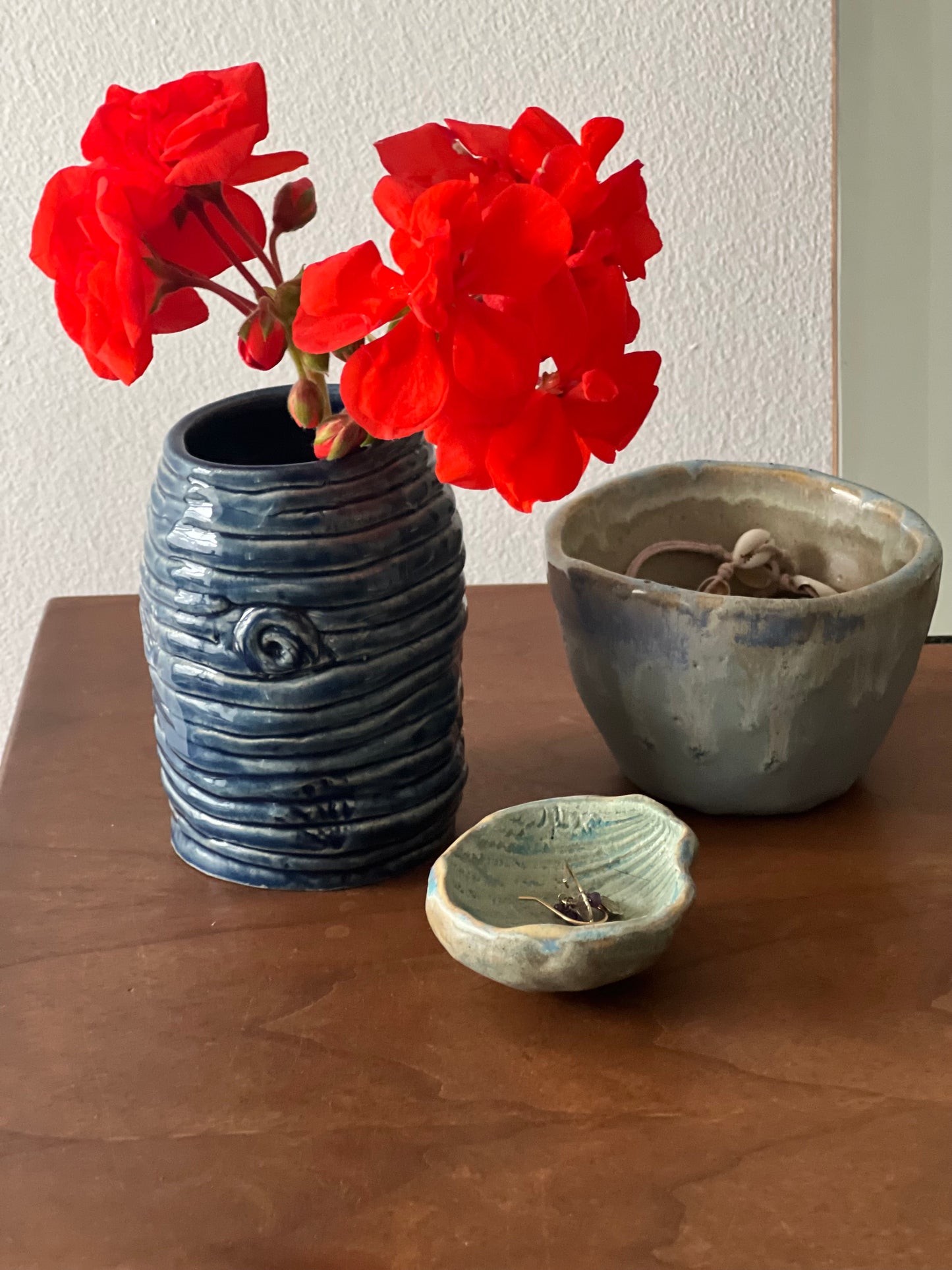 Three handmade ceramic items including a vase with red flowers on a dressing table