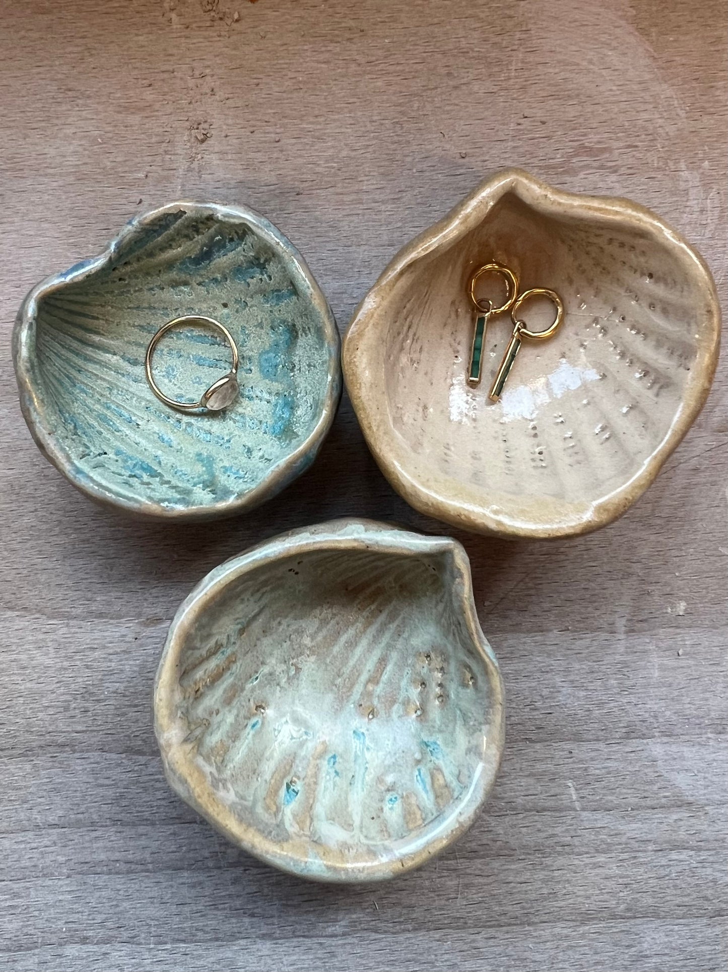 Three ceramic jewelry dishes on a wooden surface with small items inside.