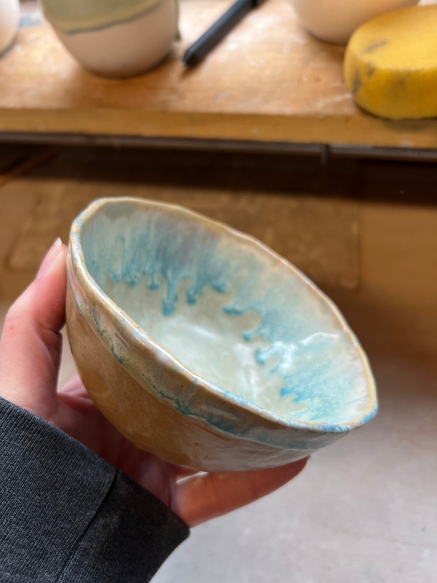 Hand holding a ceramic bowl with blue glaze in pottery studio
