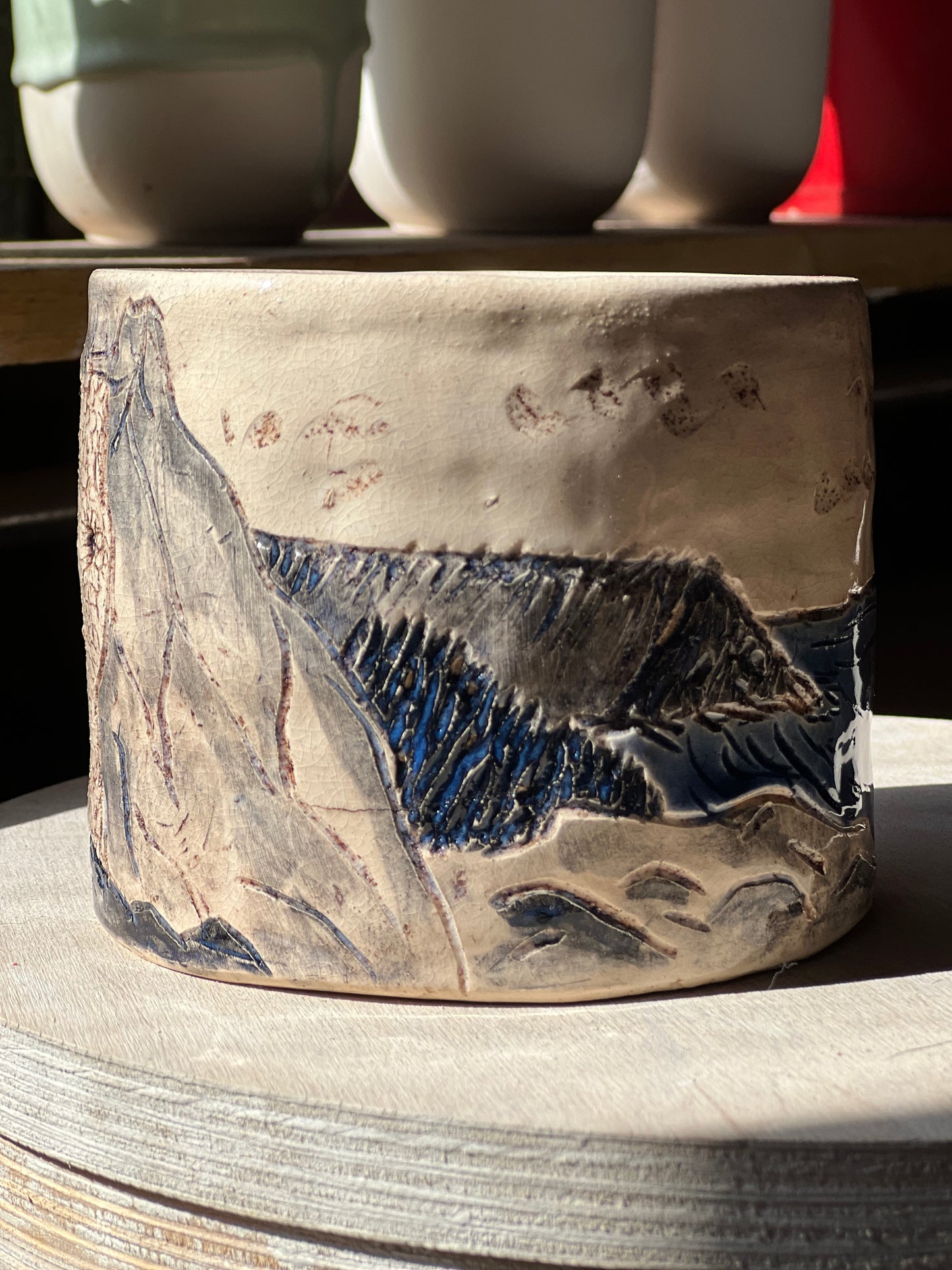 Handmade stoneware plant pot with rocks and sea design on wooden surface in pottery studio