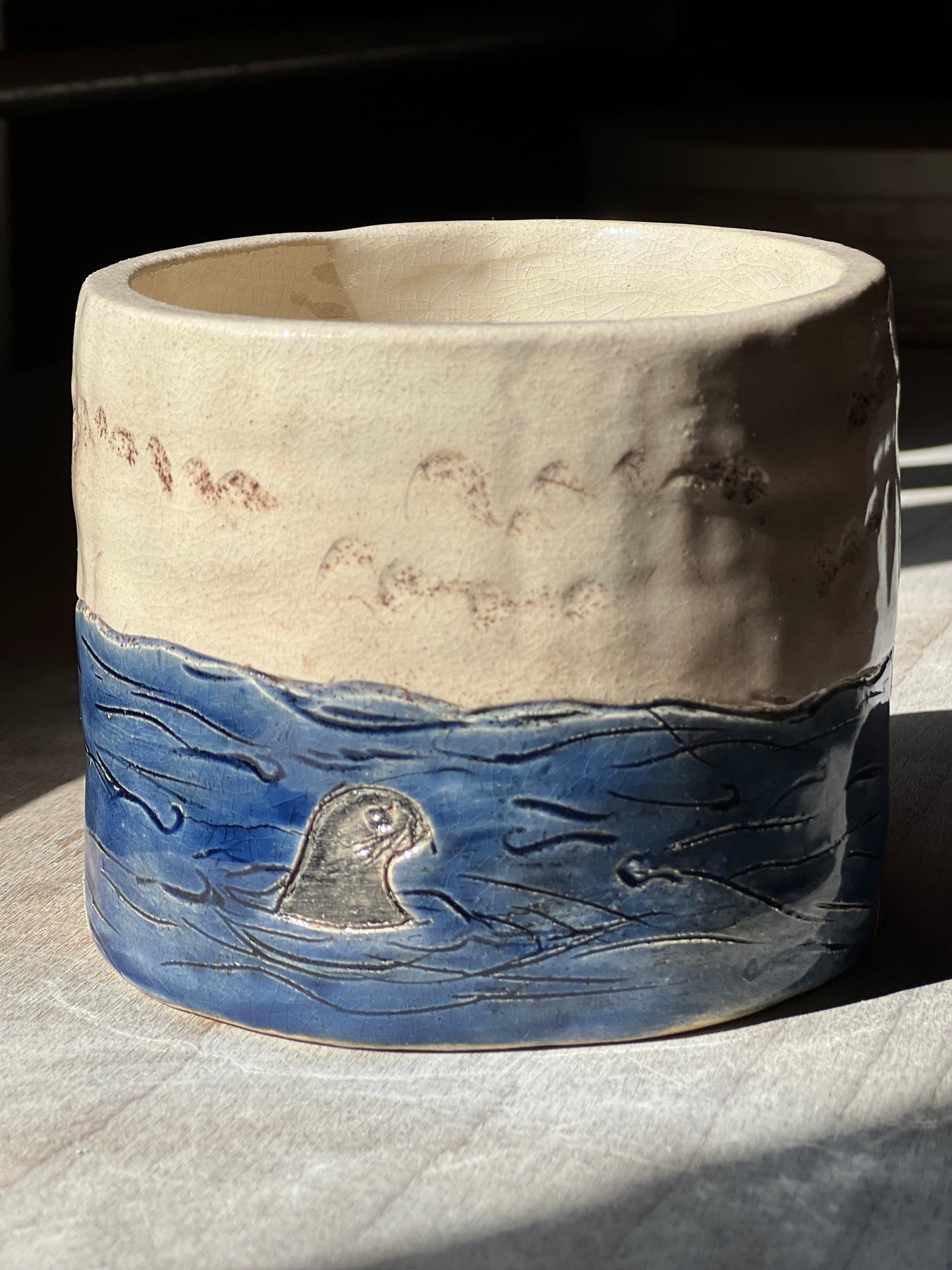 Handcrafted stoneware pot featuring hand carved design of sea and seal on wooden surface