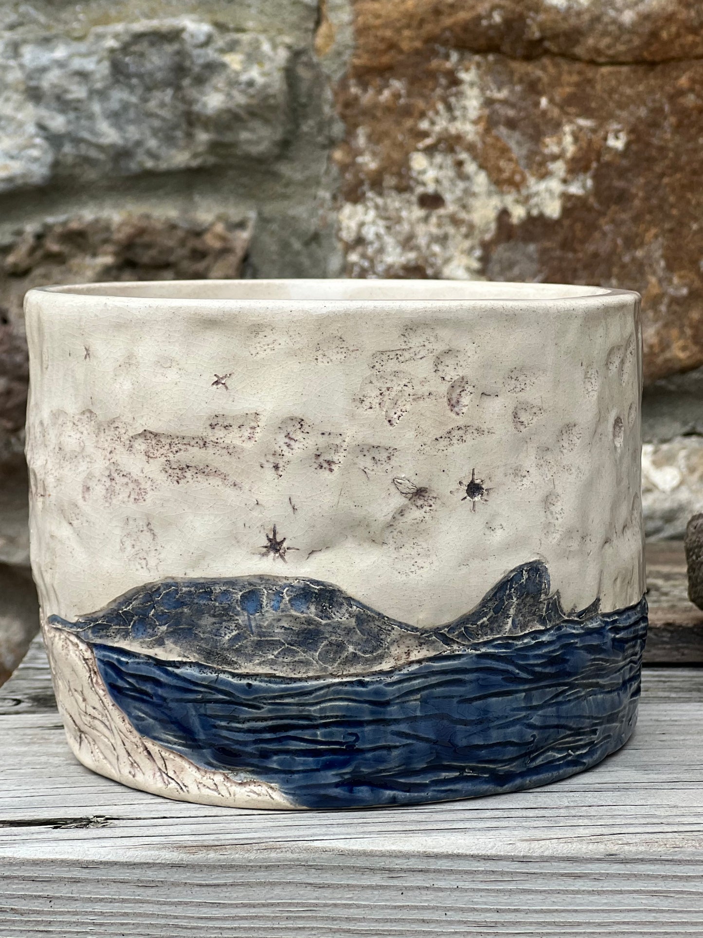 Ceramic pot with headland and starry night design against a stone wall background