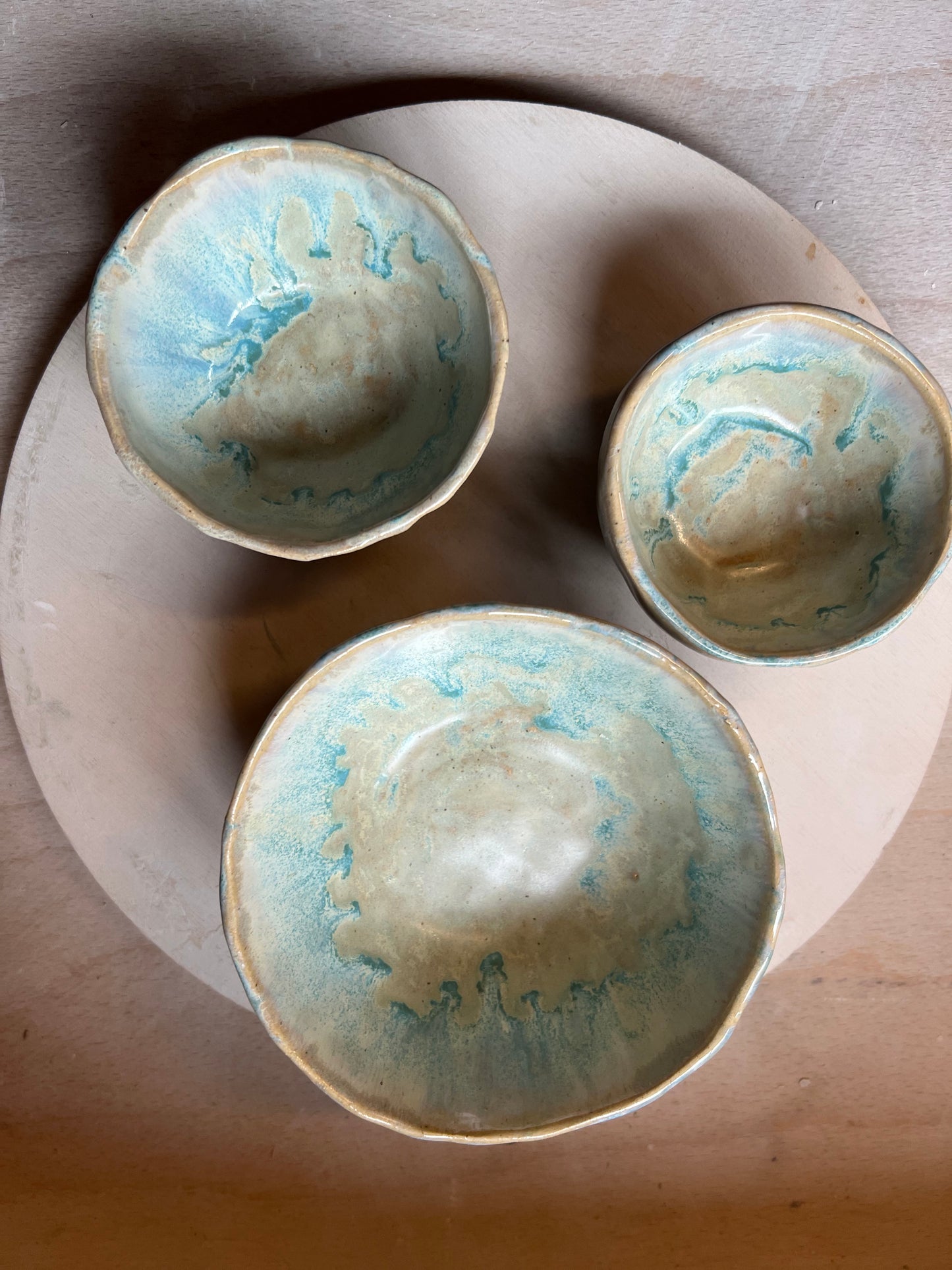 Three ceramic bowls with a blue and green glaze on a wooden tray