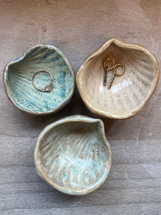 Three ceramic jewelry dishes on a wooden surface with small items inside.
