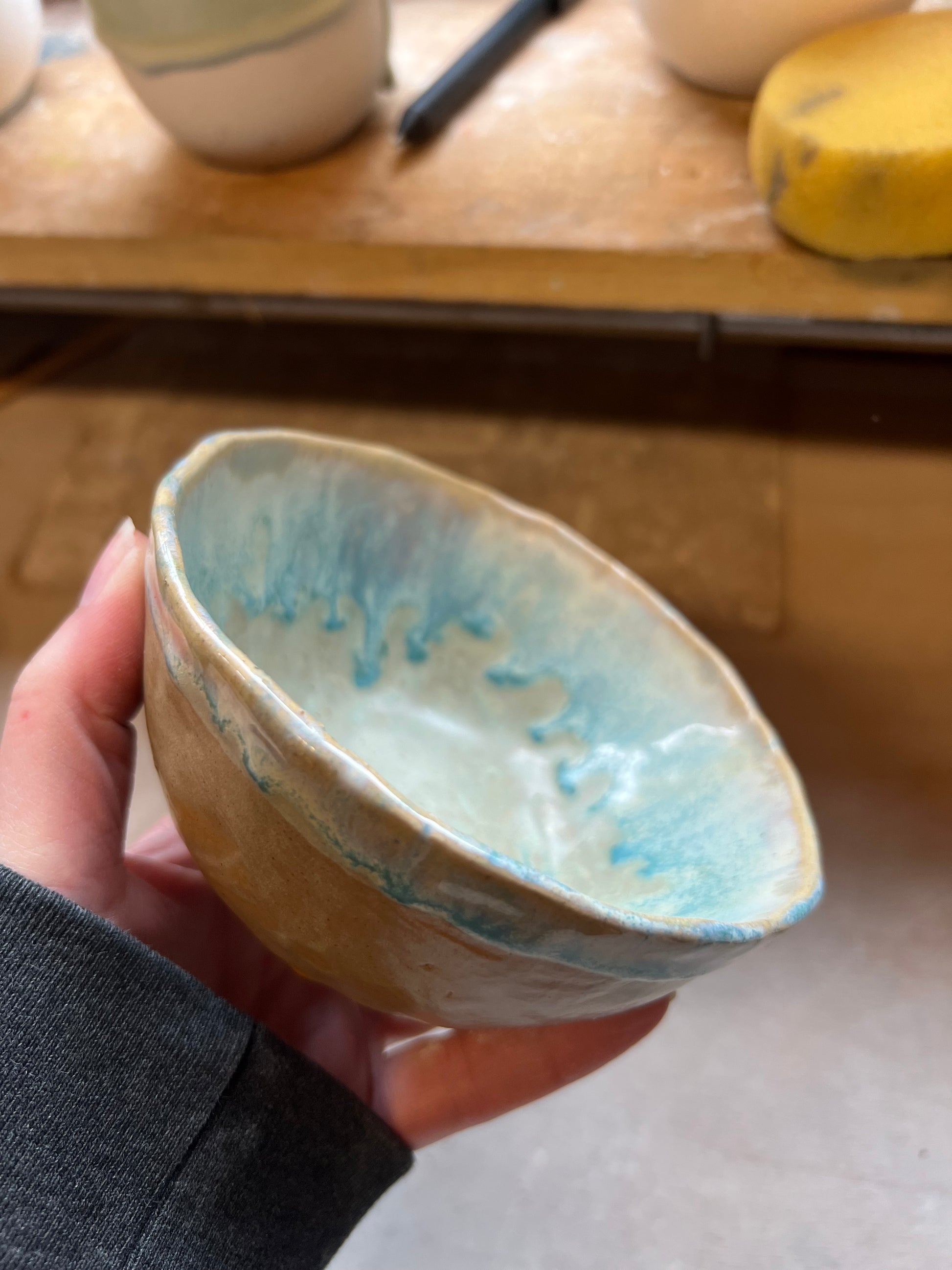 Hand holding a ceramic bowl with blue glaze in pottery studio