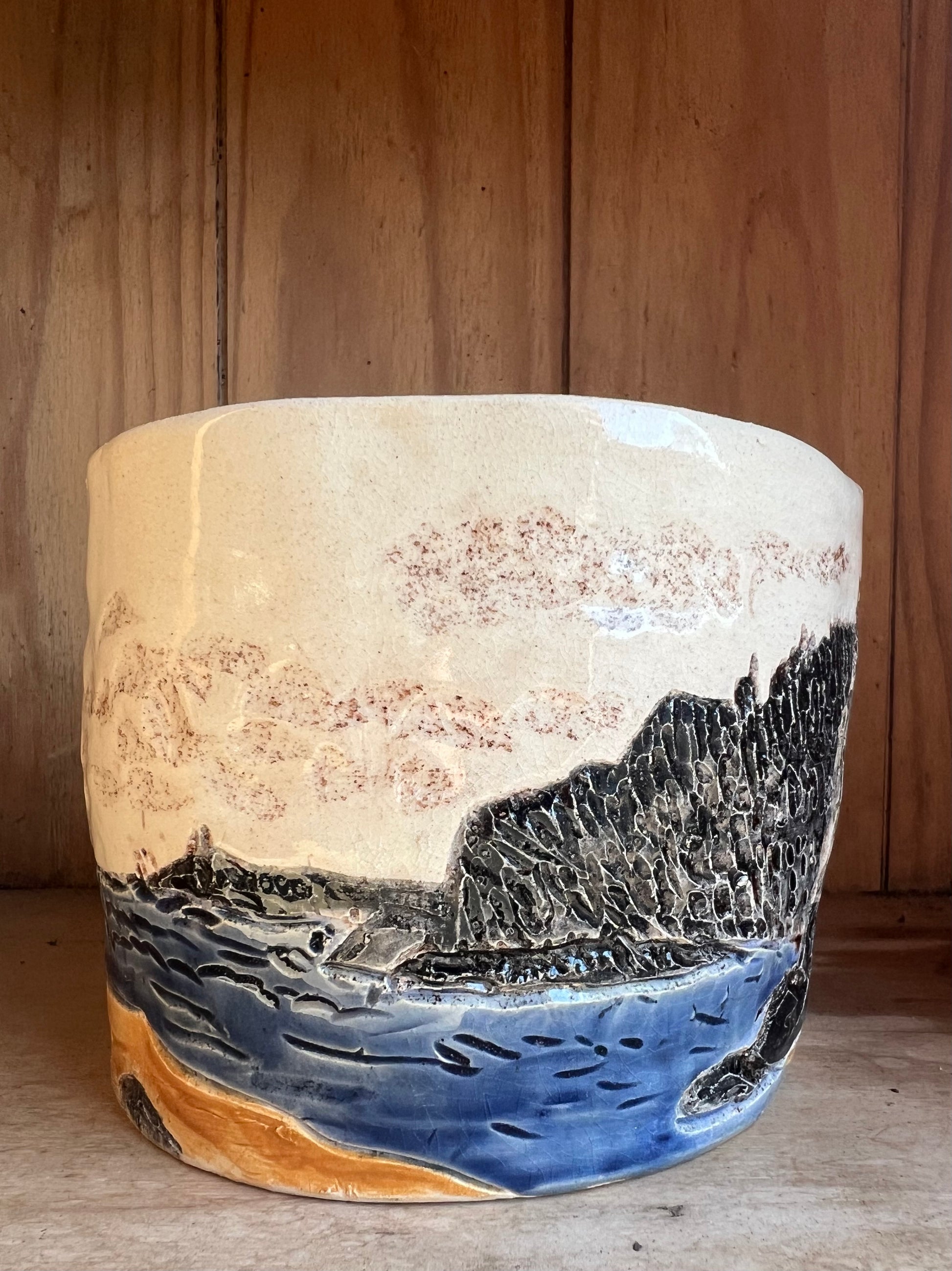 Ceramic vessel with sea and landscape design on a wooden background