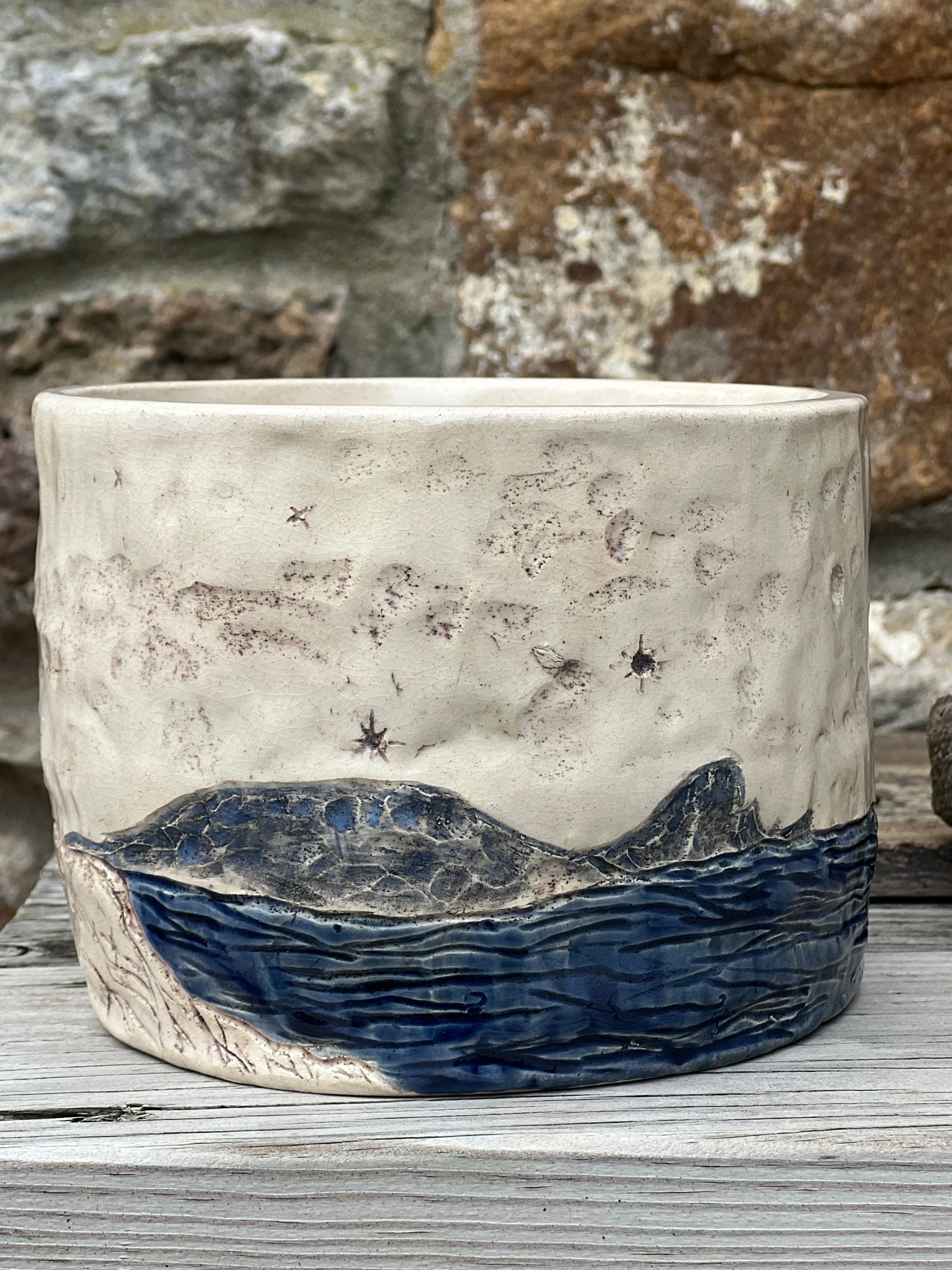 Ceramic pot with headland and starry night design against a stone wall background